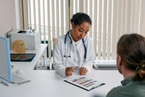 Female doctor and male patient sitting across from each other at desk in office discussing treatment options.