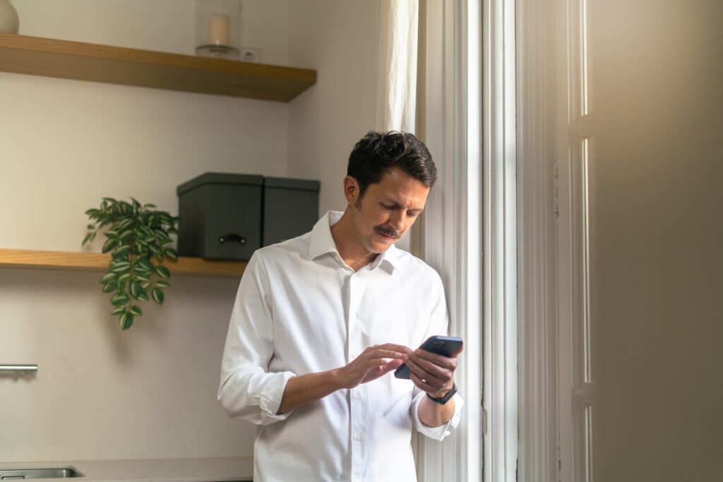 man looking at phone next to a window