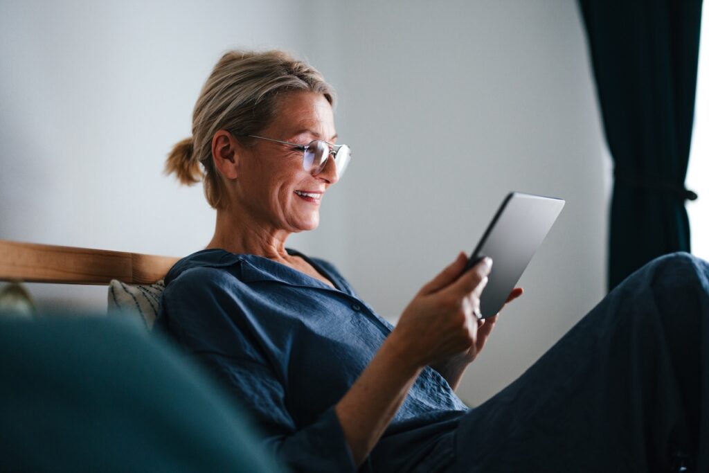older woman with glasses looking at a tablet on the couch