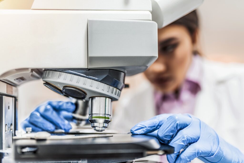 close up of a clinician scientist examining a slide under a microscope