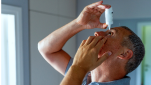 a man putting in eye drops into his eye at home