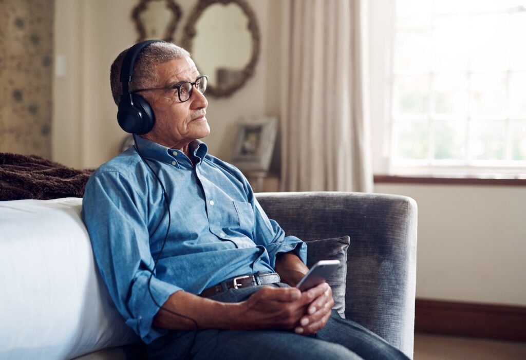 senior man using a smartphone and headphones while relaxing at home