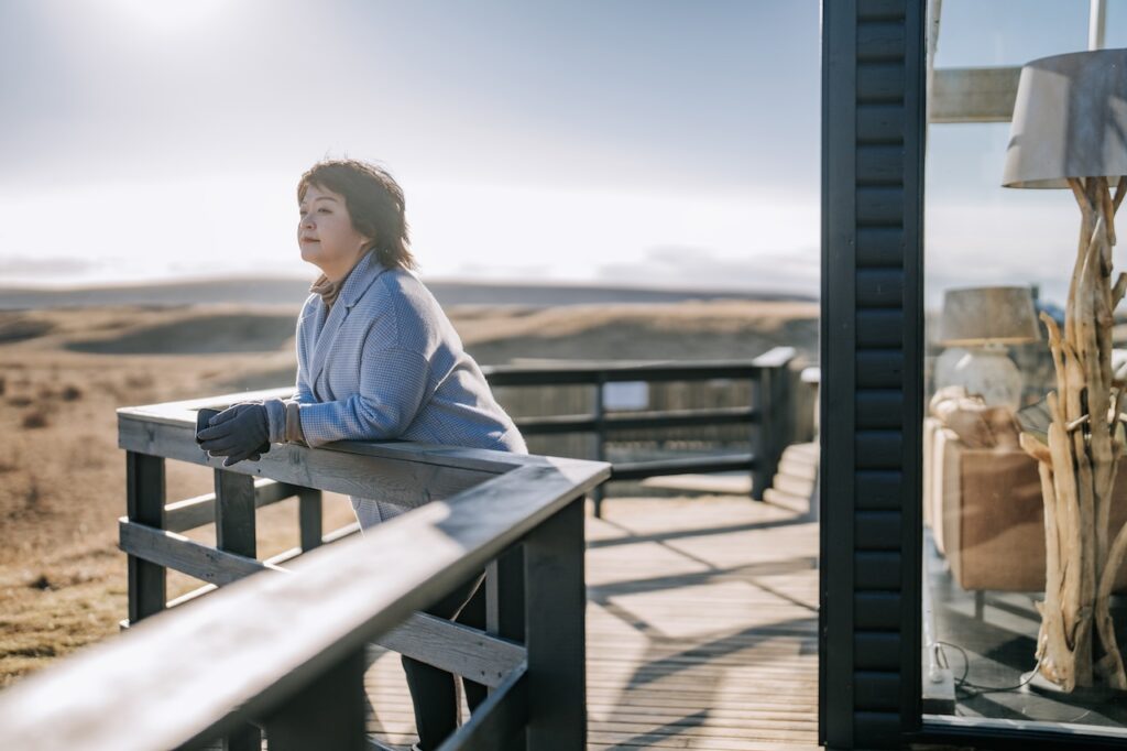 woman leaning on log cabin building terrace enjoying scenery view morning