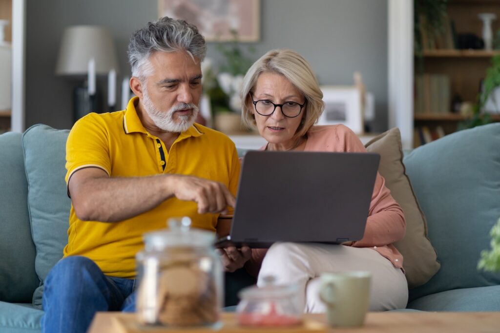 couple sitting on sofa using laptop together