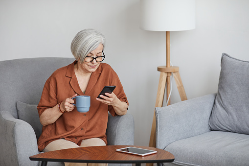 woman using smartphone and enjoying coffee indoors