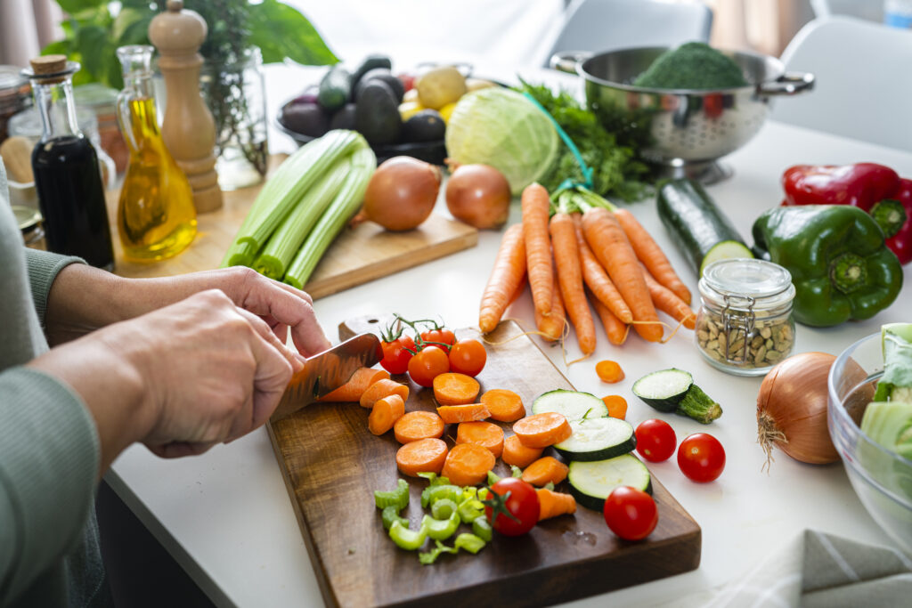 Close up of woman's hands slicing fresh carrots on kitchen counter