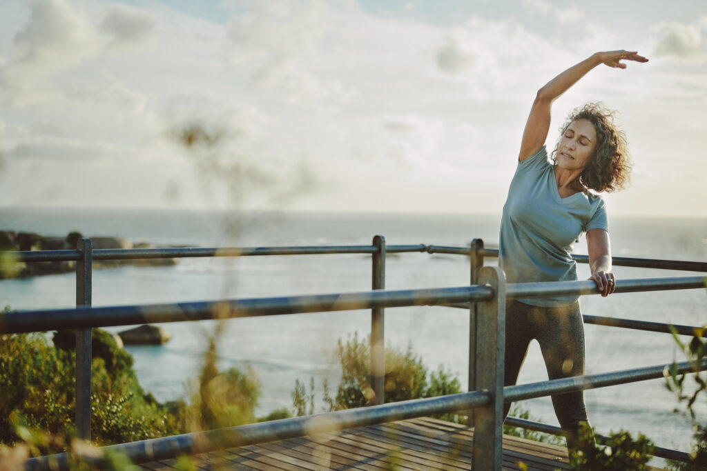 woman in sportswear stretching on the railing of a scenic viewpoint before a run by the ocean