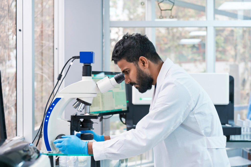 male scientist looking through microscope at laboratory