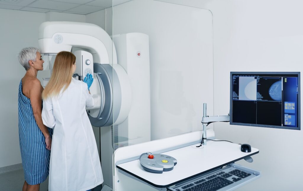 Mammogram procedure in medical clinic, mammography. Female mammologist positions mature woman at imaging machine to receive mammogram