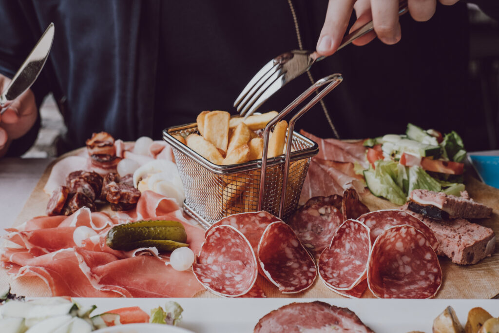 Close up of male hands holding a fork, eating cold meats platter with chips