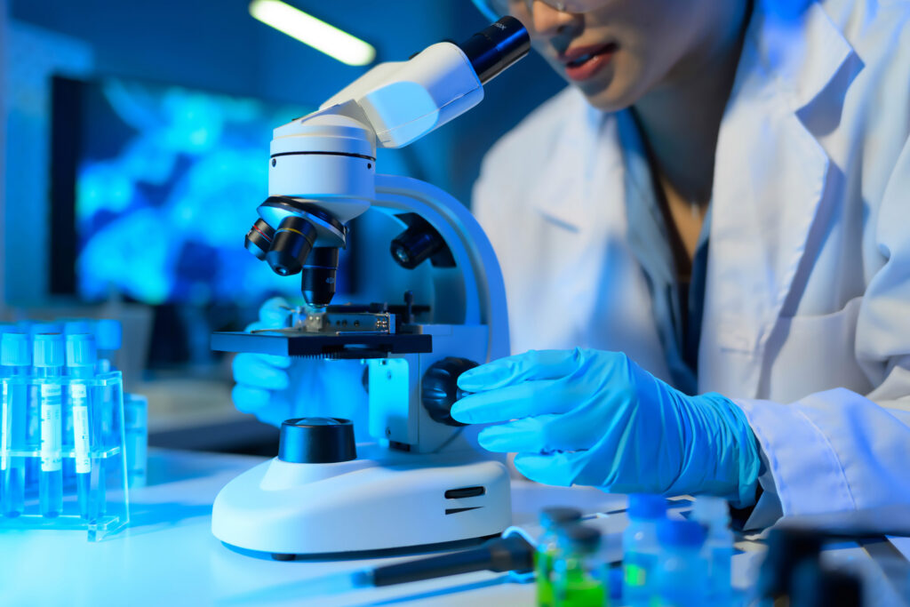 A woman in a lab coat is using a microscope to examine a sample