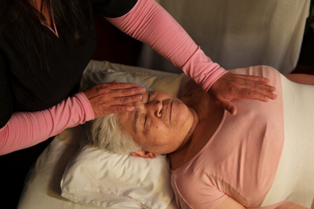 Therapist performing reiki healing treatment on senior woman lying on massage table