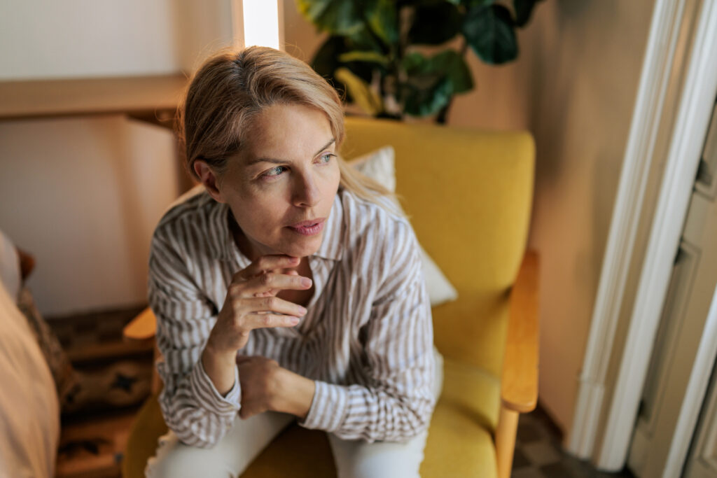 Close-up of a mature woman sitting comfortably in a yellow armchair and looking away at home.